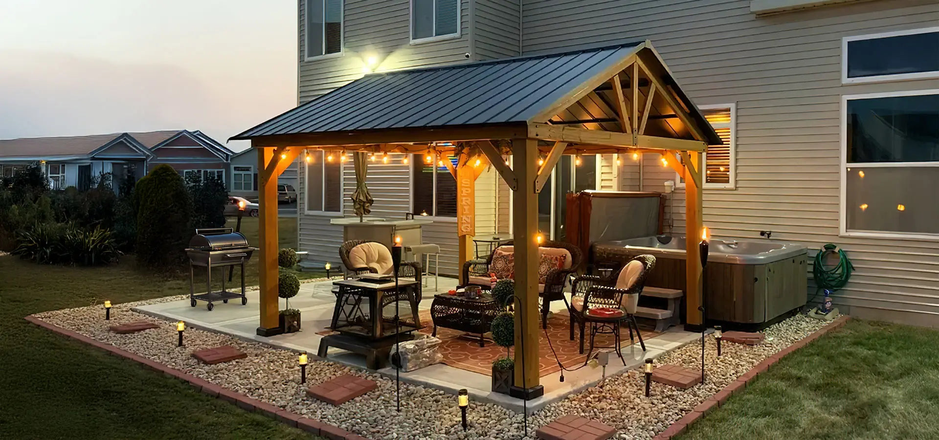 Outdoor patio with wooden gazebo, furniture, and hot tub at dusk.