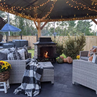 Outdoor patio with fireplace, chairs, and decorative elements under a hardtop gazebo with string lights.