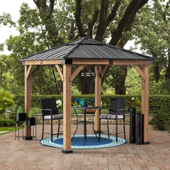 Wooden gazebo with a metal roof on a patio with outdoor furniture and plants.