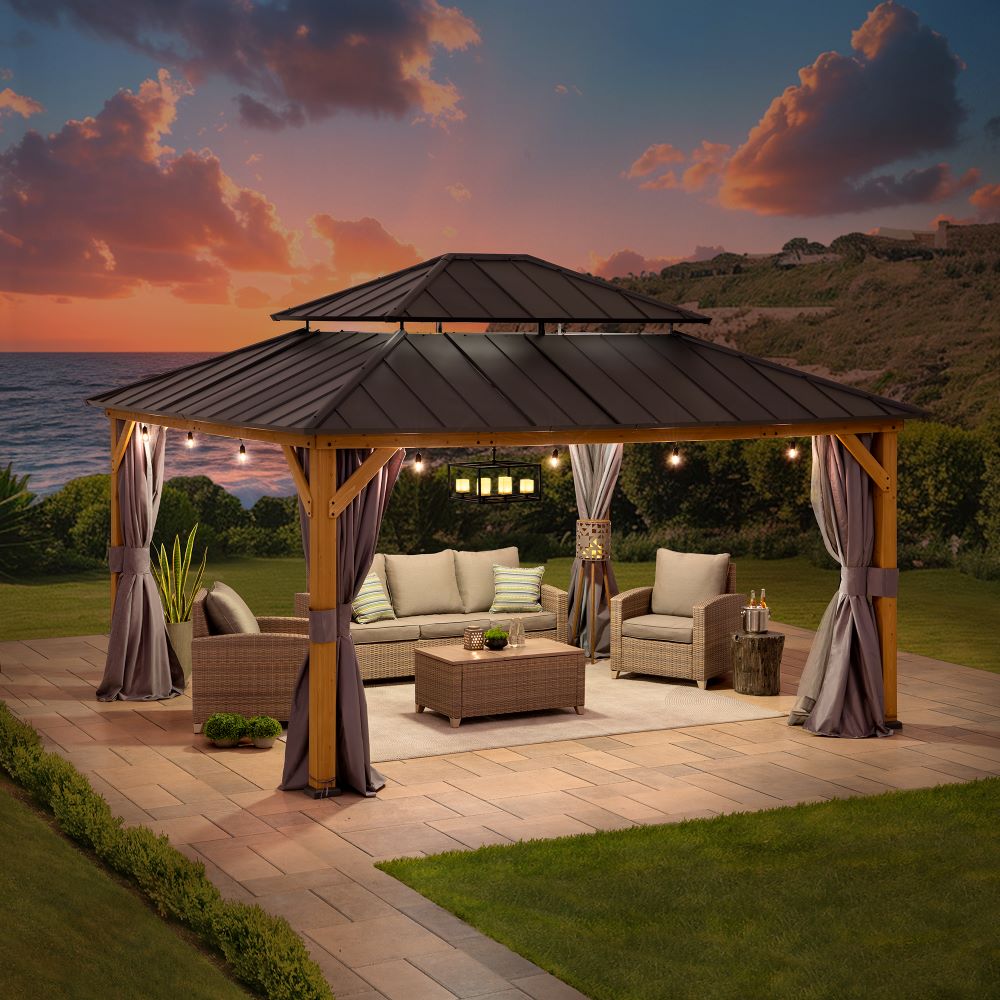 Outdoor patio with wooden gazebo, furniture, and ocean view at sunset.