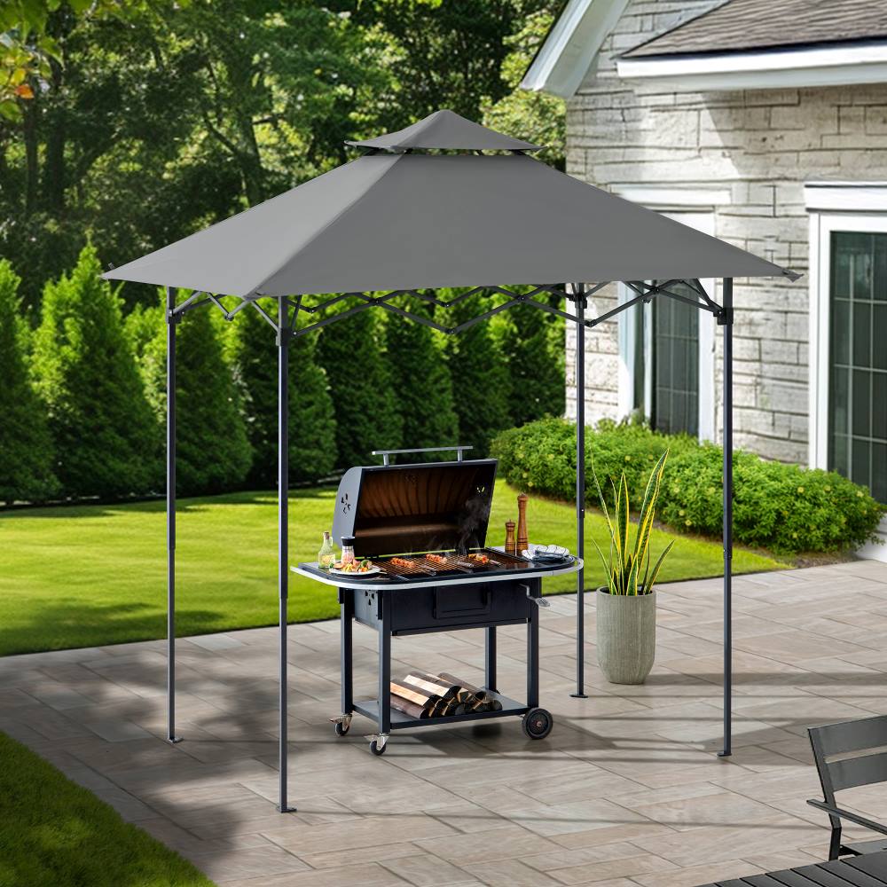 Outdoor grill under a gray canopy on a patio with a house and garden in the background