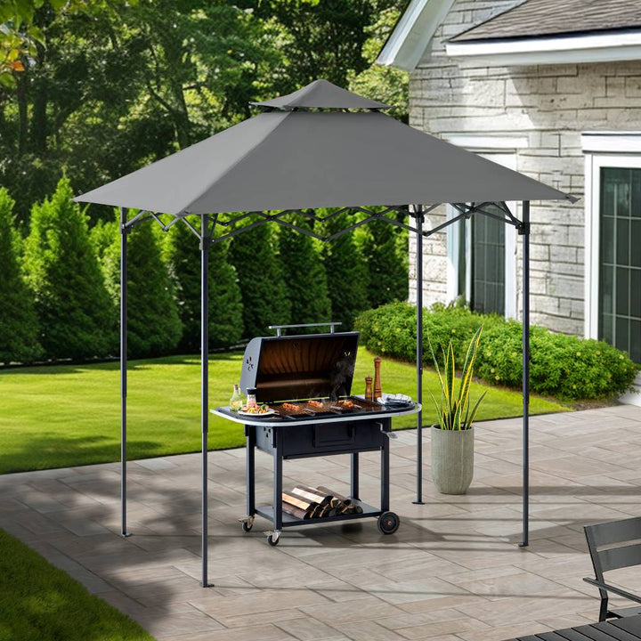 Outdoor grill under a gray canopy on a patio with a house and garden in the background