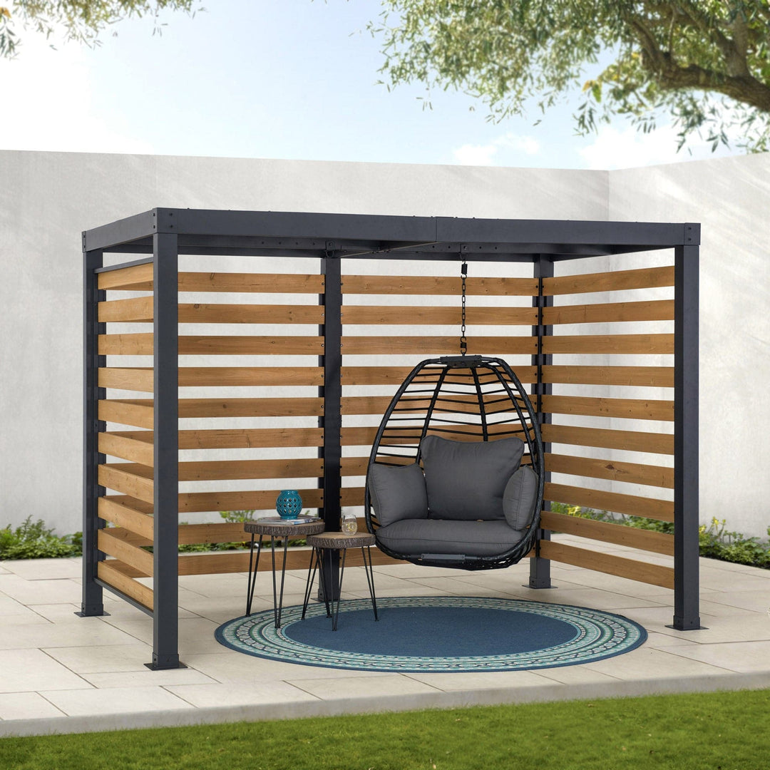 Hanging chair under a wooden pergola with a small table and round rug on a patio.