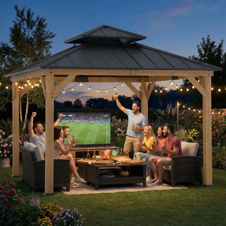 People sitting under a wooden gazebo watching a sports game on a screen, with string lights and outdoor furniture.