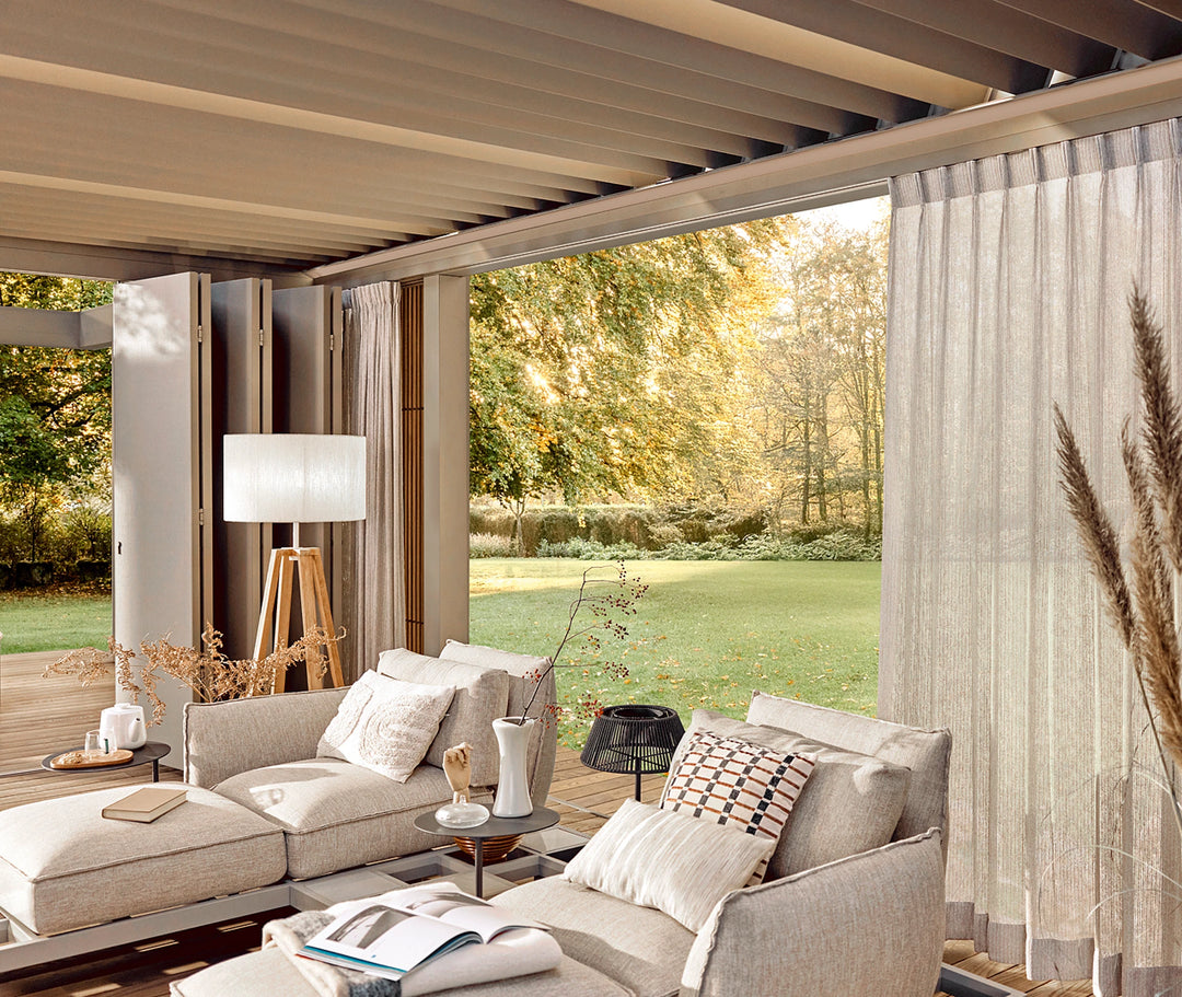 Modern patio with beige sofa, table, and decorative items, featuring a view of greenery.